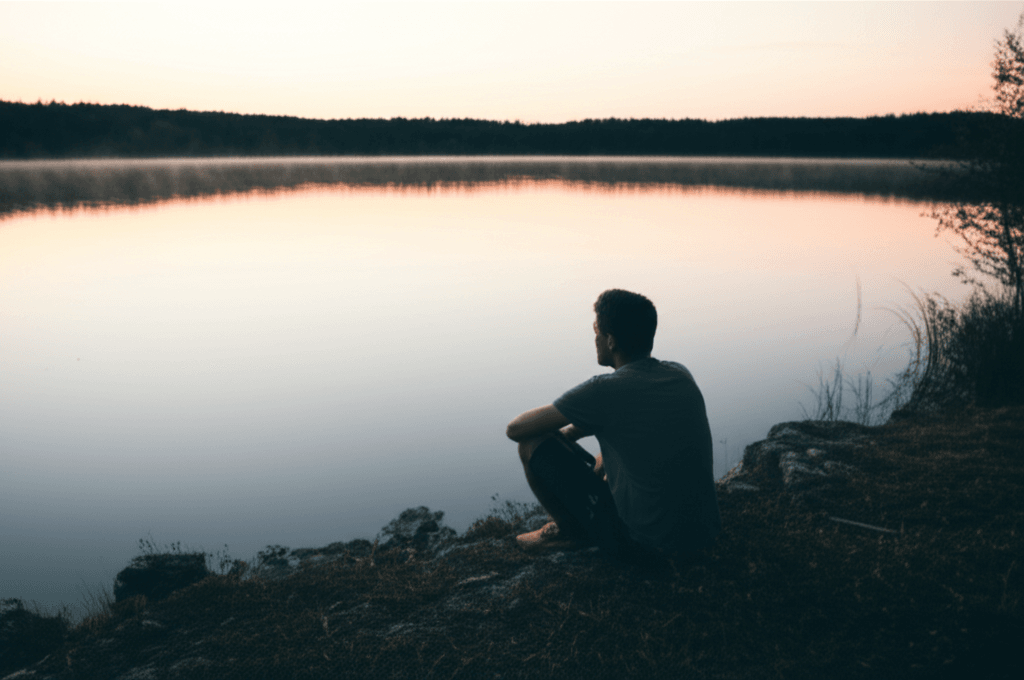 A person finding peace by sitting still and doing nothing by a tranquil lake.